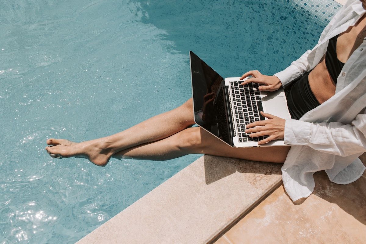 A woman sitting on the edge of a pool with a laptop on her lap