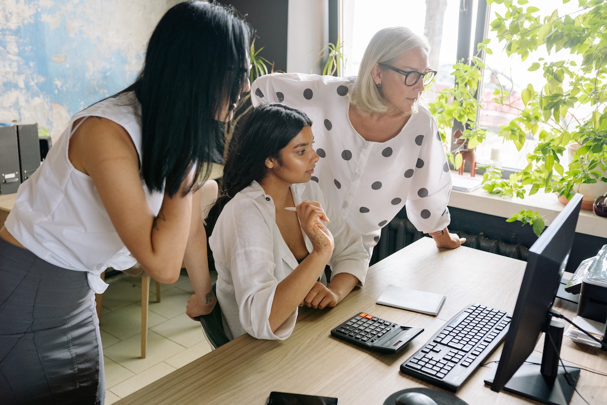 Three women looking at their hotel reservation system on a computer monitor.