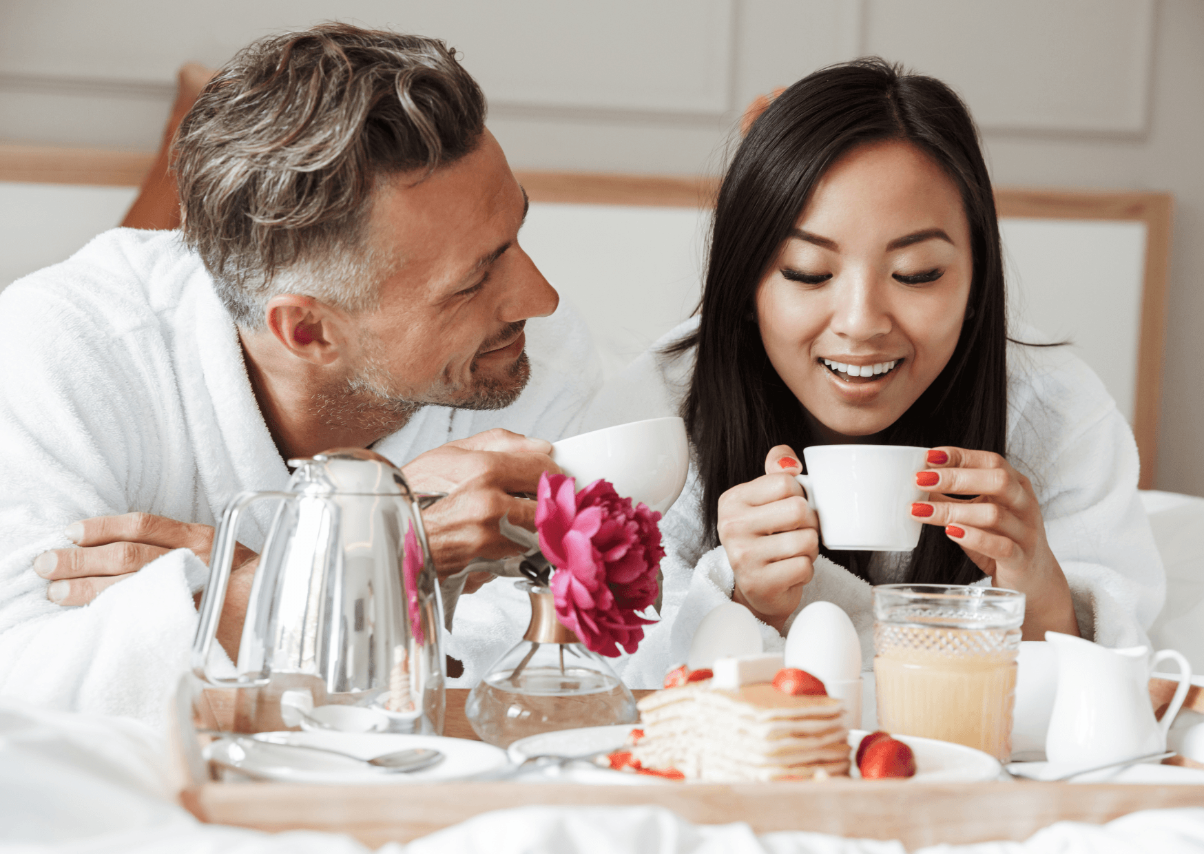A couple enjoying breakfast in bed at a hotel. 