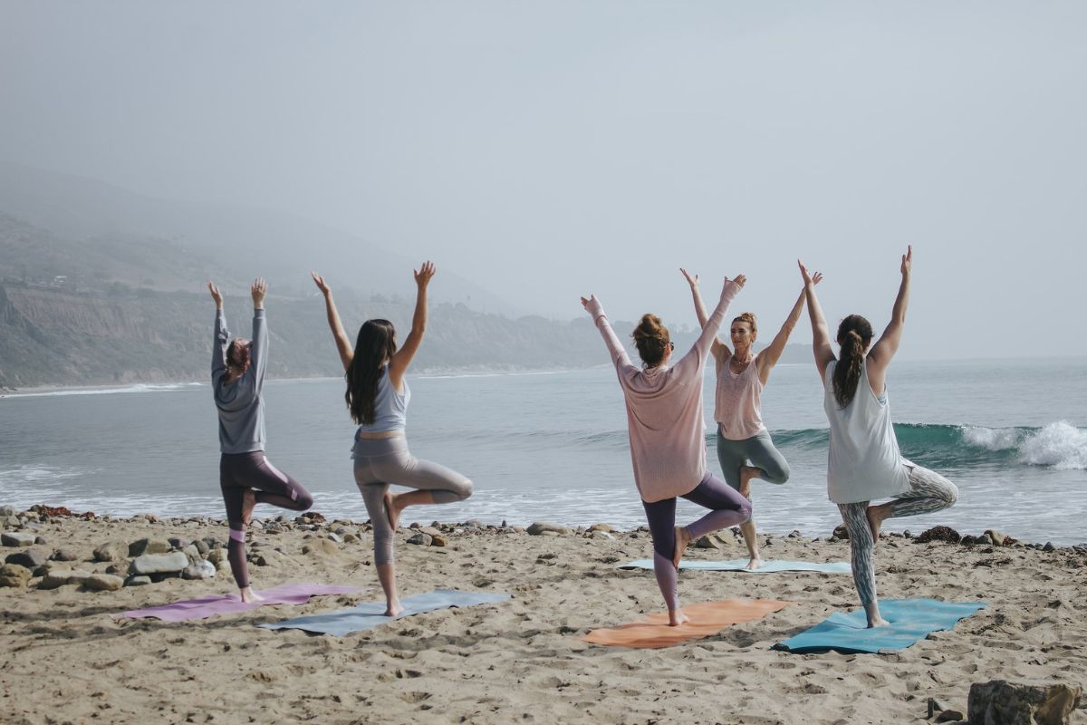 A group of women practising yoga on the beach after booking a retreat. 