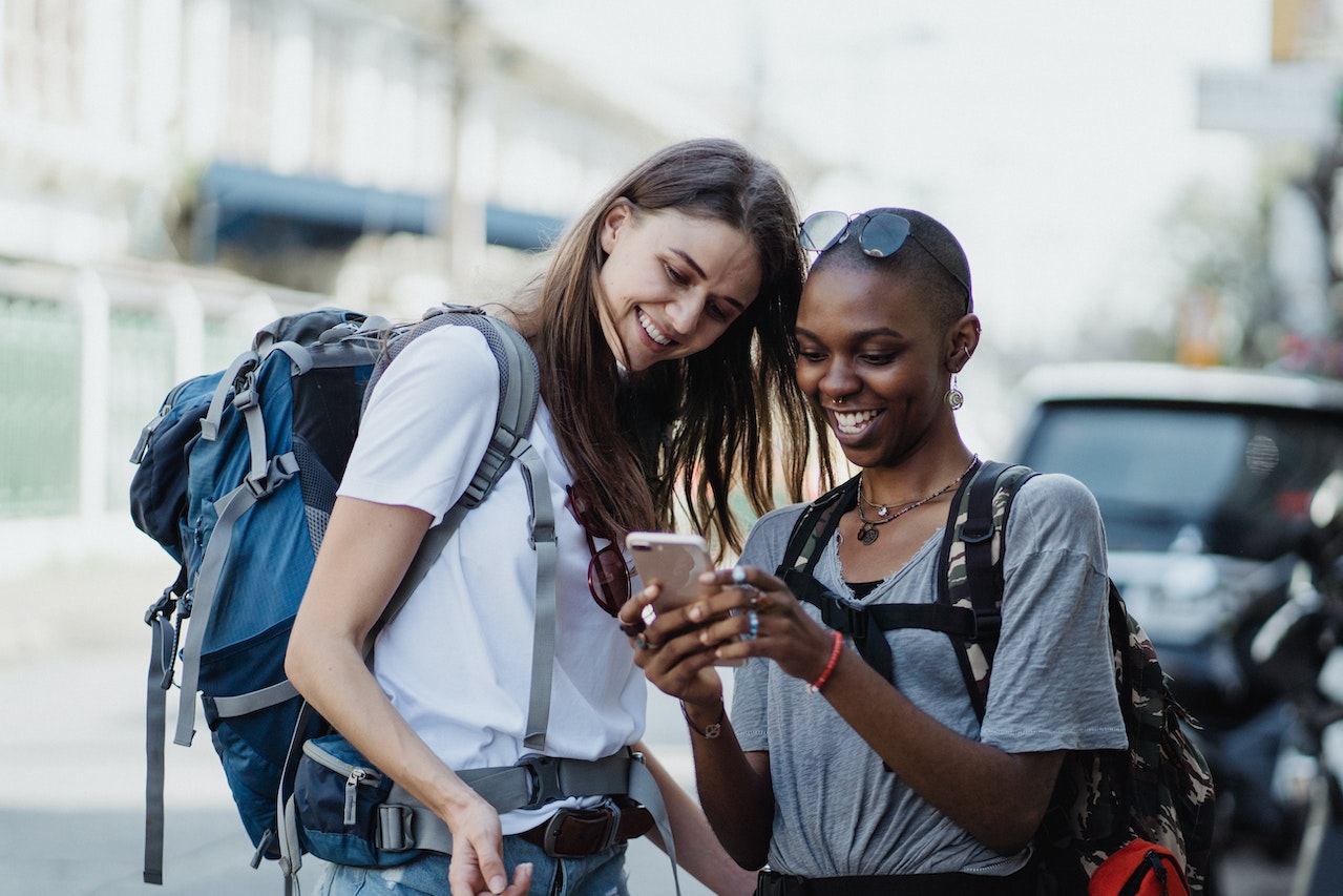 Two women with backpacks reading a pre-arrival email from their yoga retreat. 